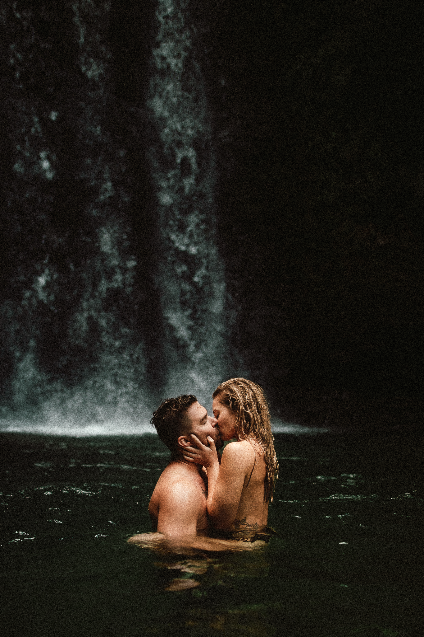 A washington state couples photographer photographing a couple in the water at the waterfall having an intimate kiss
