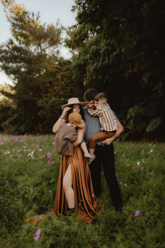 A tanquil scene unfolds in a aflower field as a mom snuggles with her son, while dad envelops the family in a warm hug, cradling his son, a blissful moment of love and togetherness being photographed by a washington family photographer