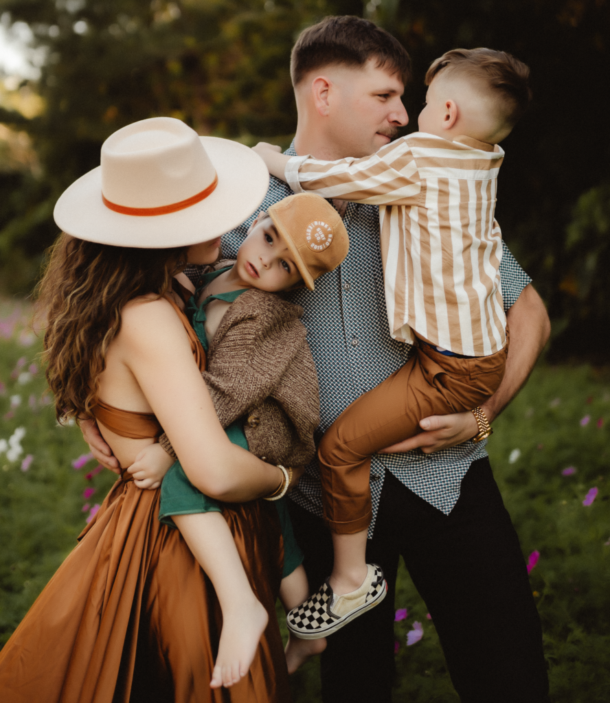 In a picturesque flower field, a fatehr gazes lovingly at one son, while the mothers adoring eyes are fixed on their other child. A heartwarming family tableau captured in nature being photographed by a Washington Family Photographer