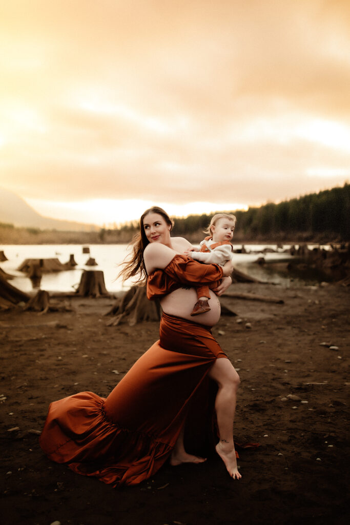 A pregnant mom holding her son at Rattle snake lake, with the wind blowing her dress and hair. Being photographed by a washington state photographer