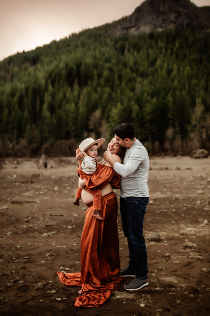 pregnant mom holding her son at rattlesnake lake in Washington state, dad is behind her grabbing her face, washington state maternity photographer 