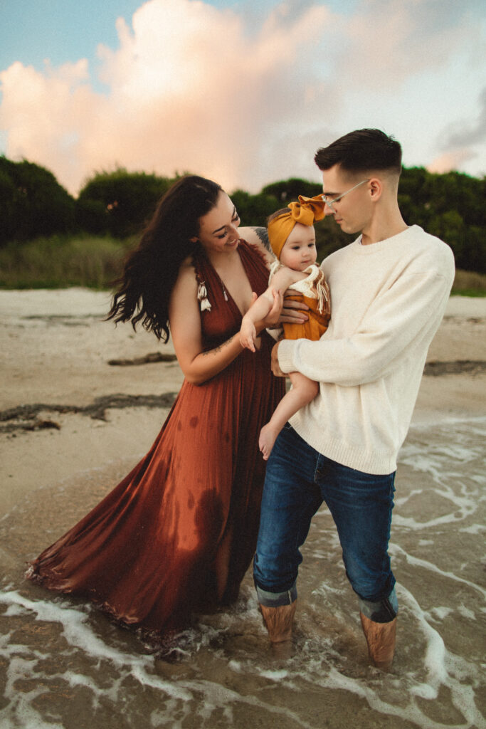 mom and dad are at the beach in washington state holding her daughter in their arms while in the water and being photographed by a washington state family photographer