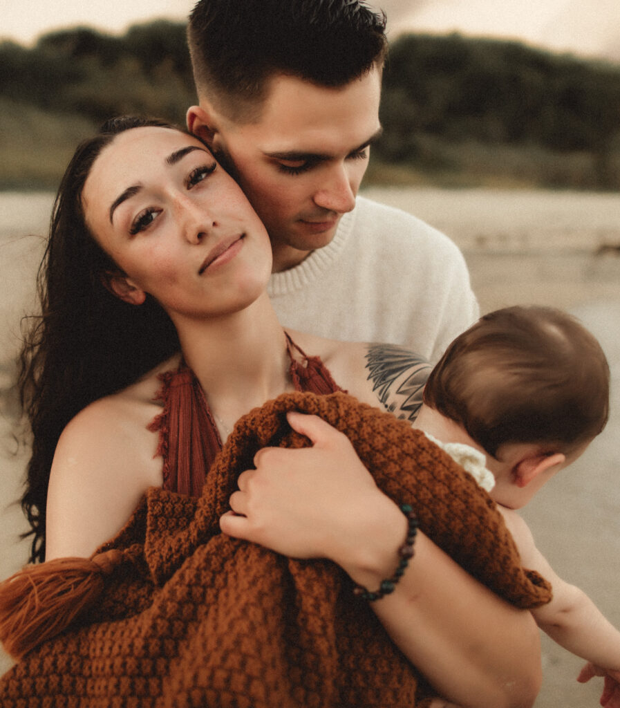 mom laying back on dad while holding and embracing her daughter in her arms while being photographed by a washington state family photographer
